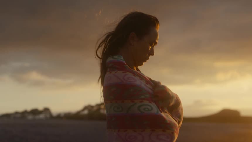 A young woman wrapped in a red blanket observes the sky at dusk outdoors