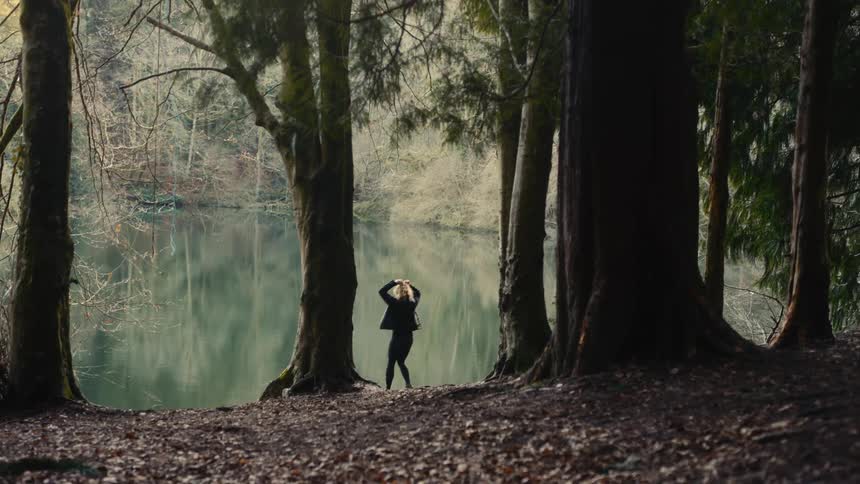 Person standing at the edge of a lake surrounded by trees