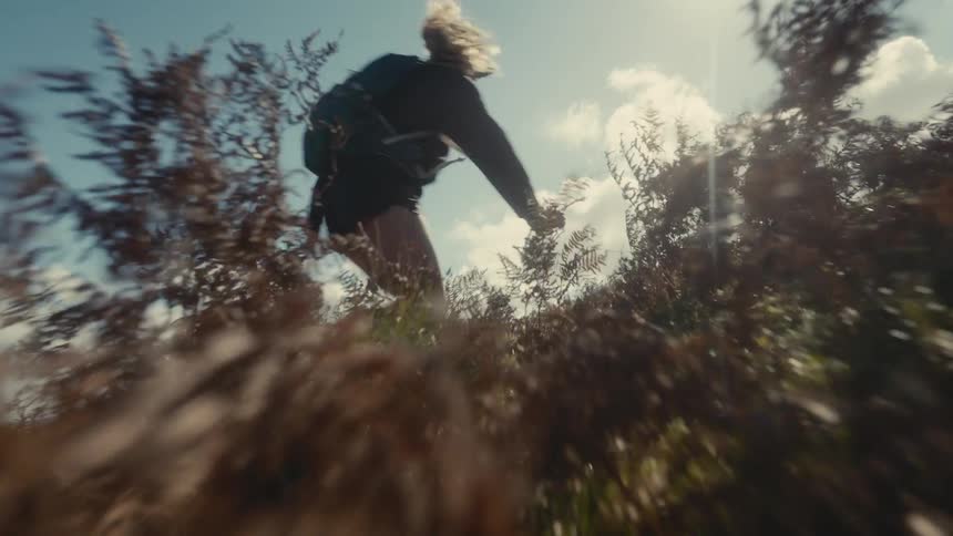A blonde woman jogs up a hill through thick foliage