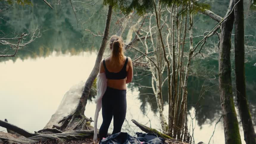 Woman taking off her shirt by a lake surrounded by trees