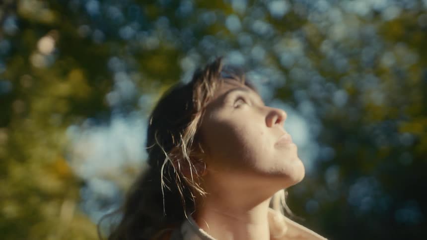 Woman looking upward in an outdoor setting with trees in the background