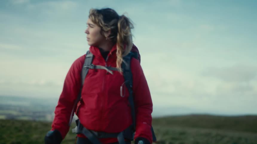 Young woman wearing a backpack holds trekking poles as she hikes across high ground