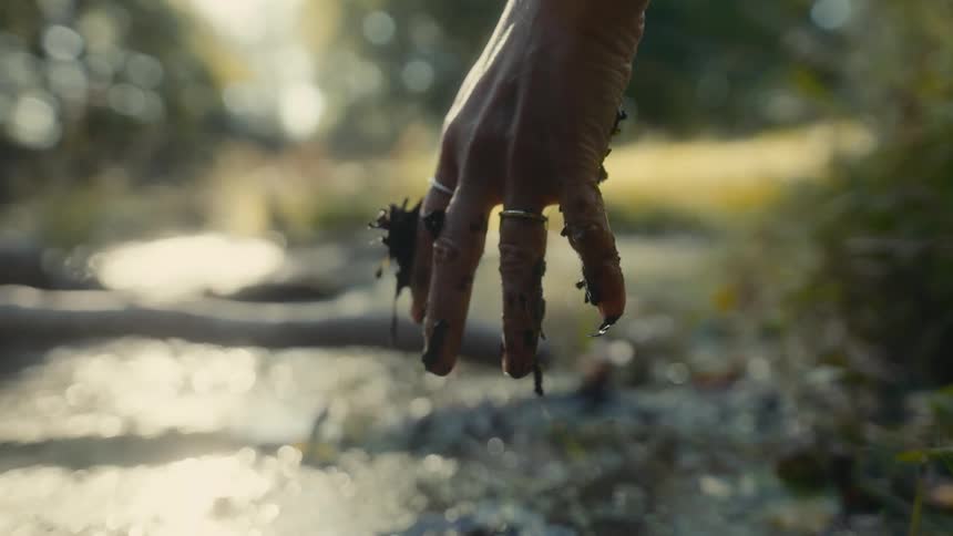 Female hand wearing rings covered in mud and dropping mud over a pond outdoors