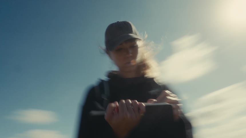 A young woman wearing a hat hikes up a highland trail pausing under the midday sun to write in a notebook