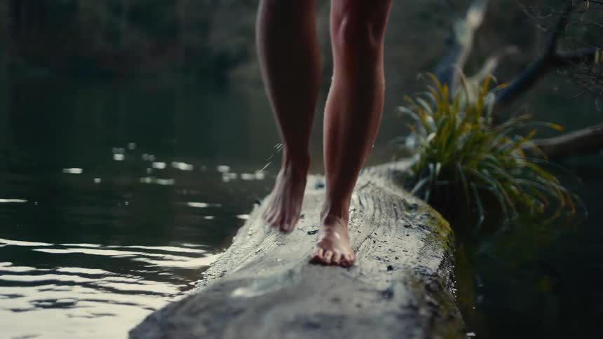 Bare legs walk on mosscovered log in calm water