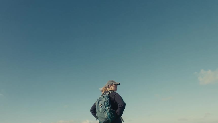 Woman with a backpack looking toward the horizon under a clear sky