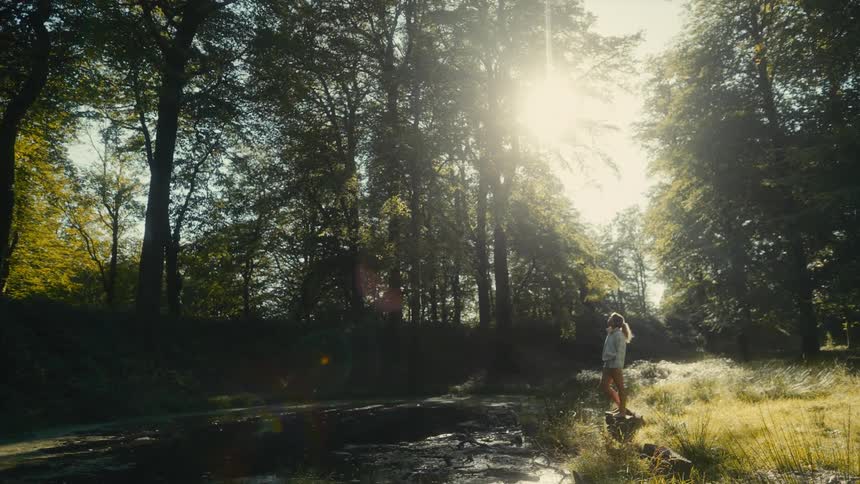 Woman stands near the water in the woods on an autumn day