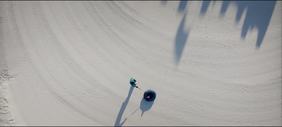 Person pulling a snow tube across white terrain seen from above