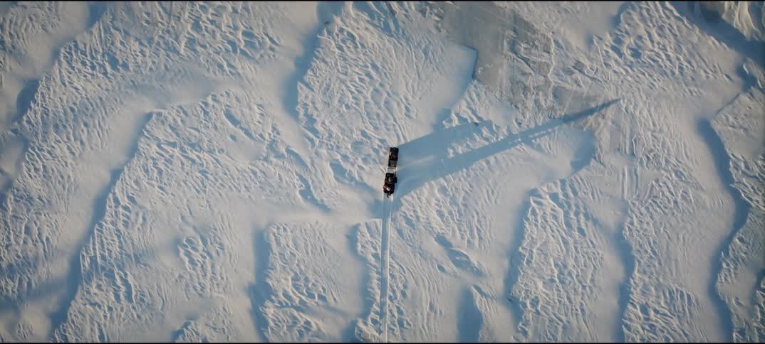 A snowmobile riding across snowy terrain at midday