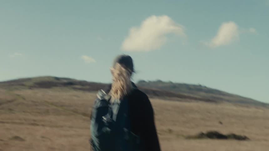 Young woman wearing a backpack walking across a rural field as she stops to look around