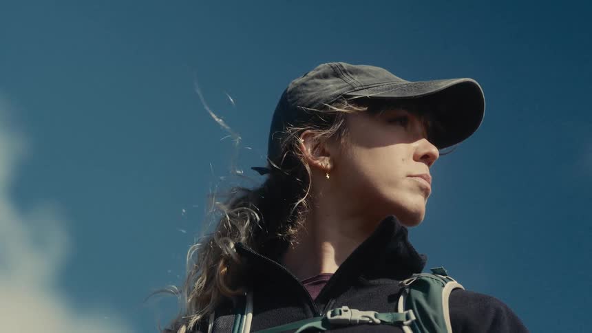 Woman wearing a cap looking upward under a blue sky