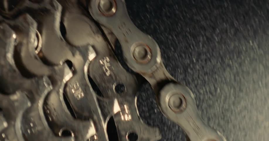 A metal bicycle chain moves over the spinning gears of a cassette