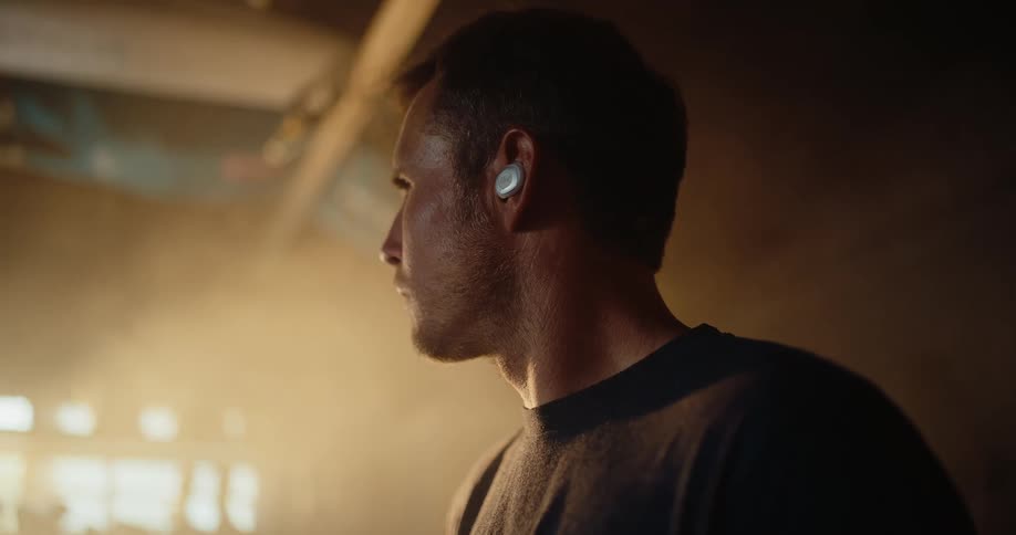 The man wears earbuds indoors