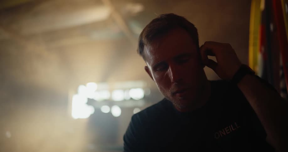 Close up of a man wearing earbuds while sitting indoors during daytime