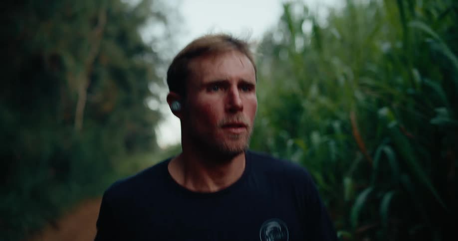 Close up of a man jogging outdoors through a path in a grass field during daytime