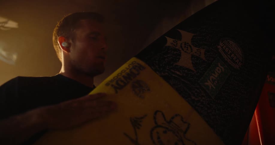 Man holding a yellow surfboard with drawings while wearing an earbud
