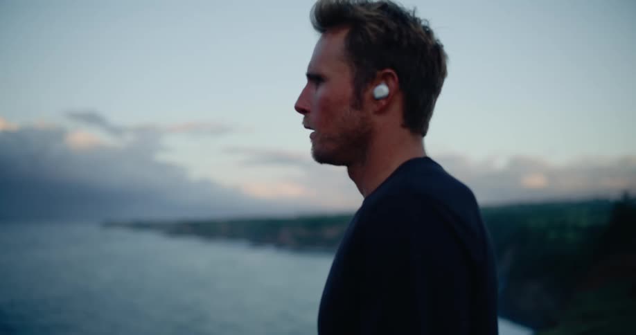 Close up of a man jogging outdoors towards and away from a lake shore during daytime