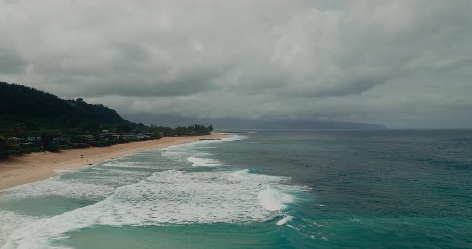 Beach with a small group of people on it with the ocean to one side and buildings and vegetation to the other outdoors during day time