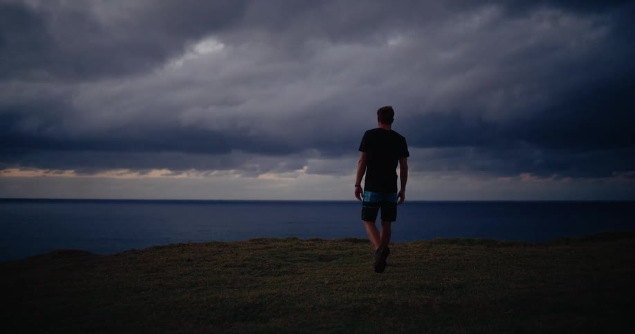 A man walking outdoors on a coastal grass field towards the ocean during daytime
