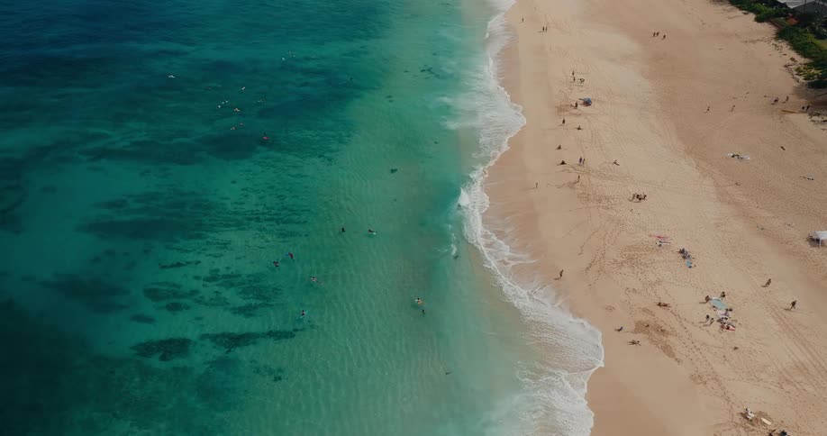 Aerial of multiple people swimming and having fun at the beach during daytime