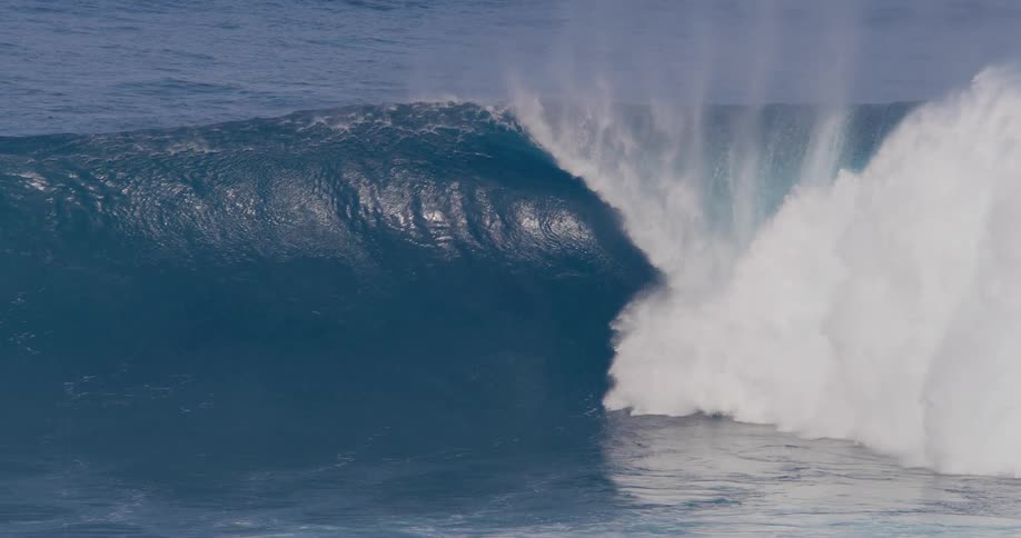 A person surfing a wave in the ocean at midday while other surfers stand by watching