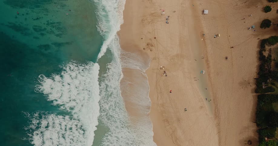 Powerful blue ocean waves build up and break violently towards the camera forming a large white foam barrel under a hazy sky