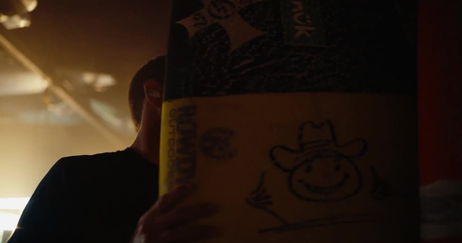 Close up of a young man selecting a surfboard from a board rack indoors during daytime