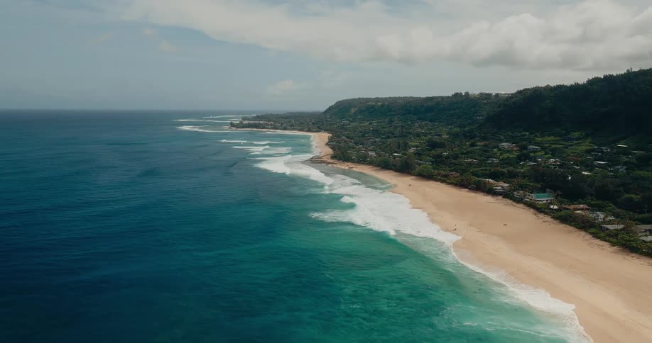 A coastline with a coastal town along the shore as light waves hit at midday