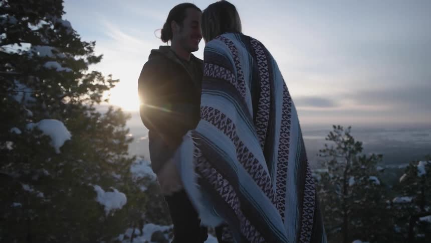 A man and woman embrace a snowy forest