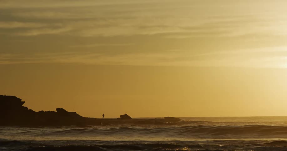 Person standing on coastal rocks at sunset