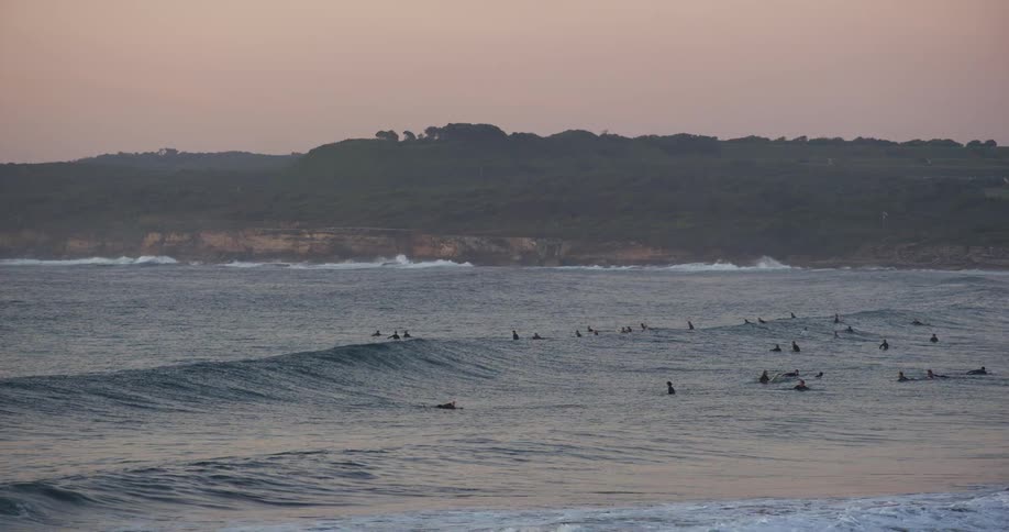 A group of people swimming in the ocean near the beach at midday with gentle waves rolling through the water