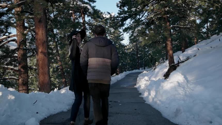 A man and a woman walk down a path in the snow with trees on either side