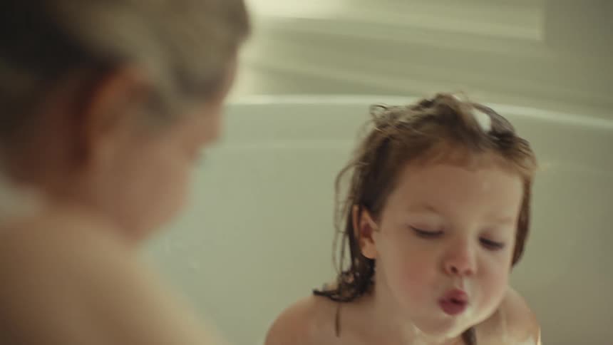Mother and child interact with foam in the bathtub