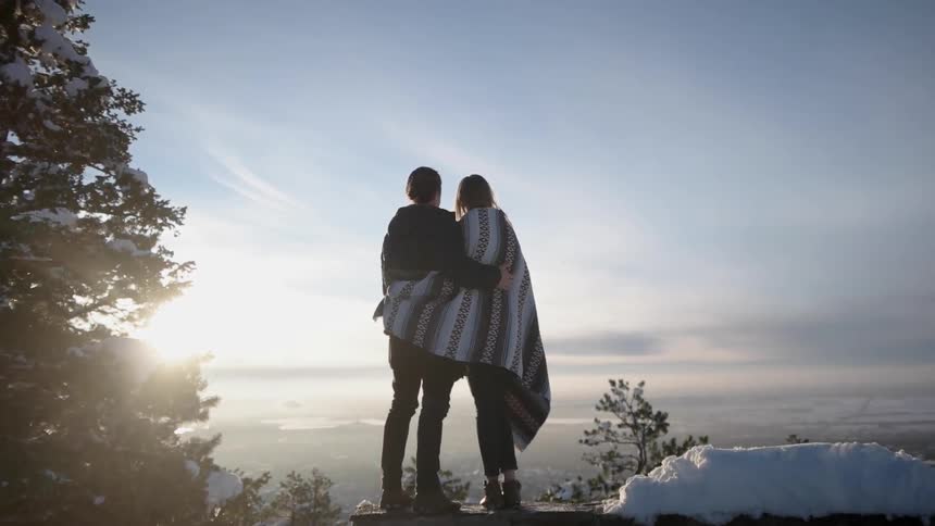 Two people stand on a cliff hugging