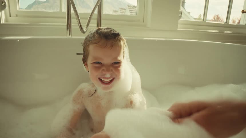 Mother and daughter playing with soap lather while bathing in a tub indoors during daytime