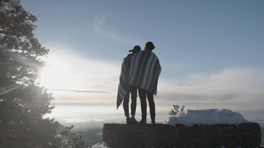 A man and woman share a blanket in the snowy mountains