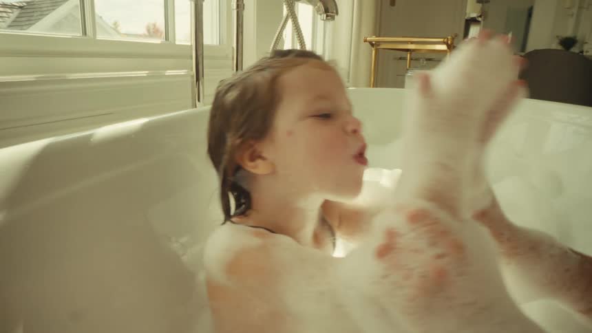 Small girl and young adult woman smiling and playing with the soap foam while the girl is on the bathtub indoors during day time