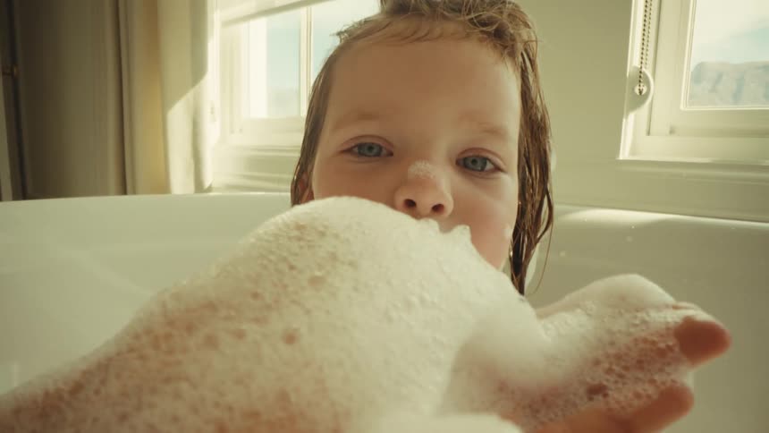 Child in a bathtub holding foam with an emphasized facial expression
