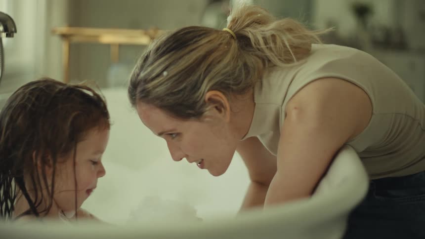 Mother leaning over the bathtub touching her forehead to her daughters during bath time
