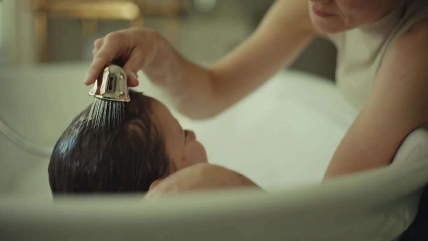 Close up of a young mother washing her daughters hair in a bathtub indoors during daytime