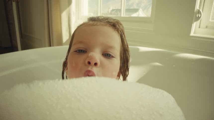 A girl playing in a bath tub with bubbles