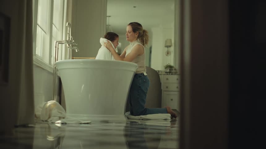 Woman kneeling and drying the child with a towel beside the bathtub