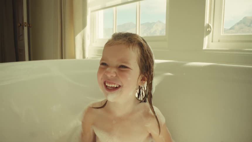 Smiling child in a bathtub with foam and an open window in the background