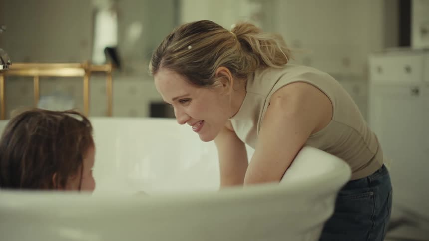 Woman leaning over the bathtub looking at the child