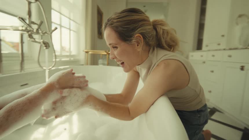 Mother and daughter playing with soap lather while bathing in a tub indoors during daytime