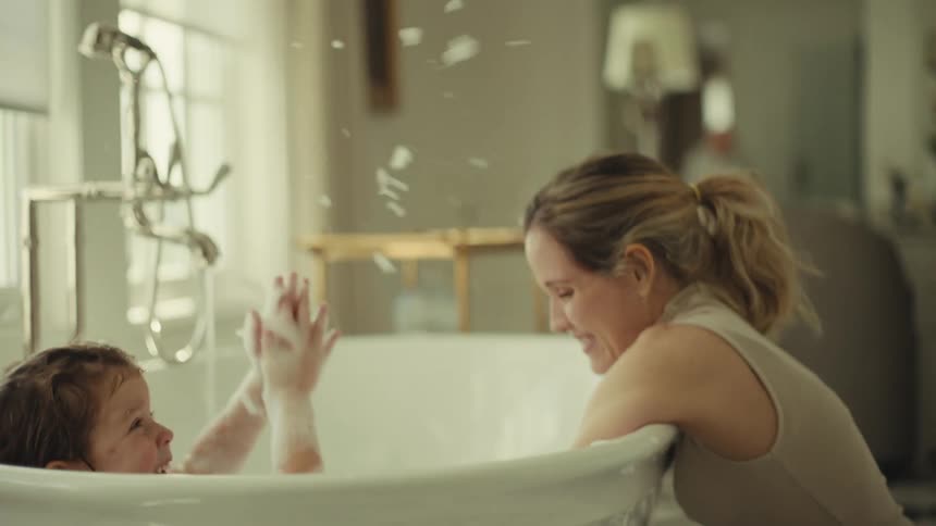 Mother and daughter smile while playing with foam during bath time