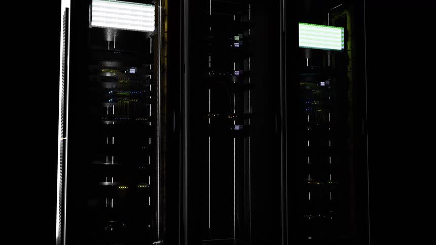 In a dark room large led panels atop two server racks slowly power on gradually illuminating the complex hardware and blinking indicator lights within the data center
