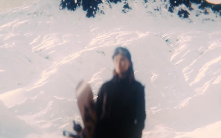 Young woman standing on a snow covered mountain looking around as she holds a snowboard