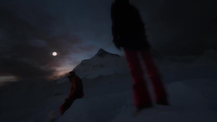 Two people in winter gear stand by a small fire on a snowy mountaintop under a dark cloudy night sky with a bright full moon