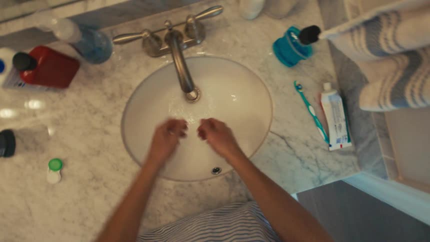 Hands being washed in a bathroom sink equipped with hygiene items